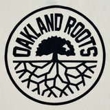 Detailed close up front image of ecru t-shirt with Oakland Roots SC crest in black.