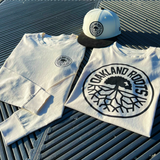 Ecru short sleeve tee, Ecru long sleeve tee and chrome cord new era fitted with black roots crest displayed on textured outdoor surface.