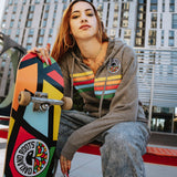 Model outside with skateboard wearing gunmetal heather full zip hoodie with colored stripes and full-circle Roots SC mosaic logo on wearer's left the chest.