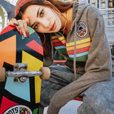 Model outside with skateboard wearing gunmetal heather full zip hoodie with colored stripes and full-circle Roots SC mosaic logo on wearer's left the chest.