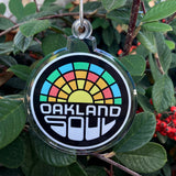Acrylic Oakland soul crest ornament with silver string hanging on tree.