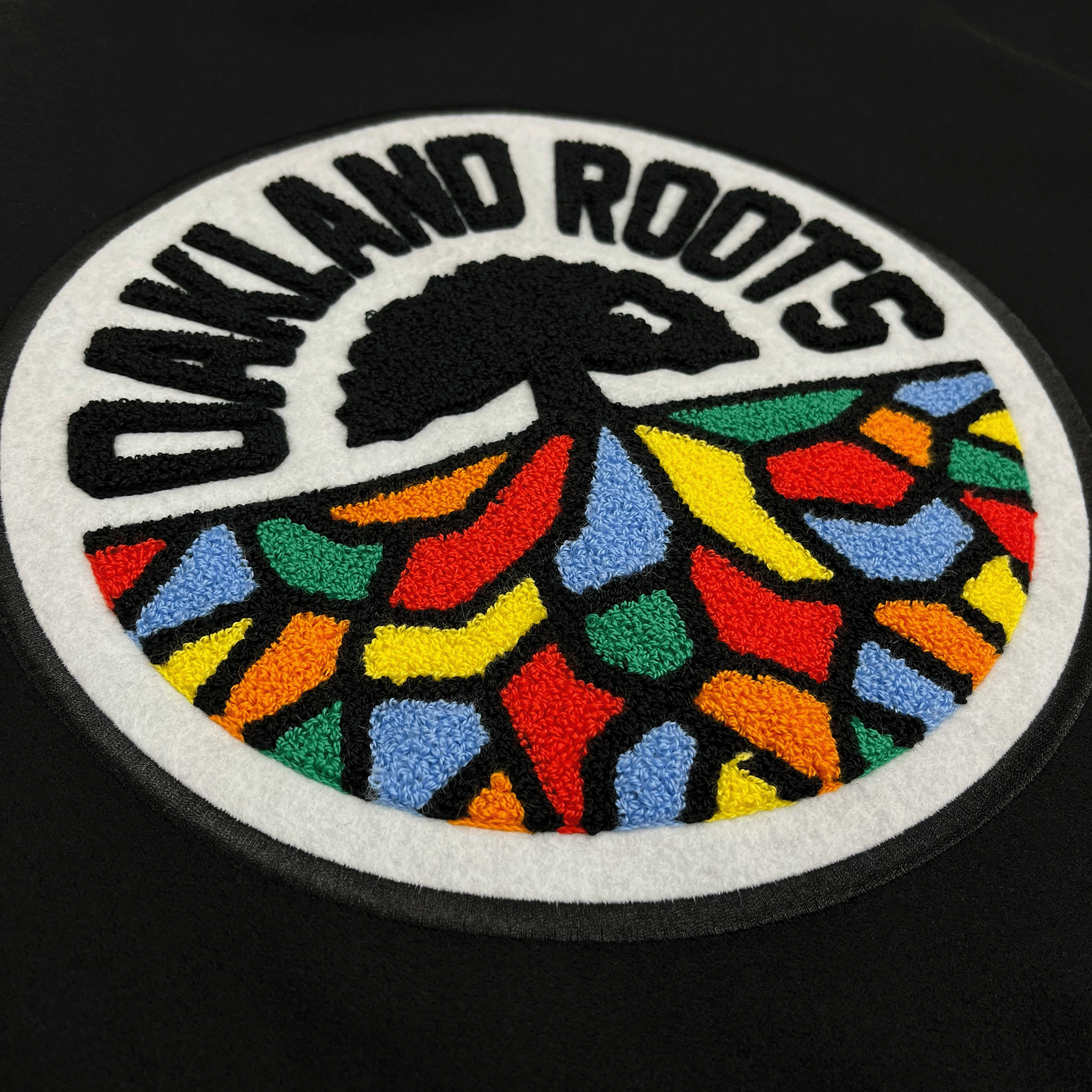 Side-angled close-up of large round full-color 3D Oakland Roots lagoon on the back of a black varsity jacket.